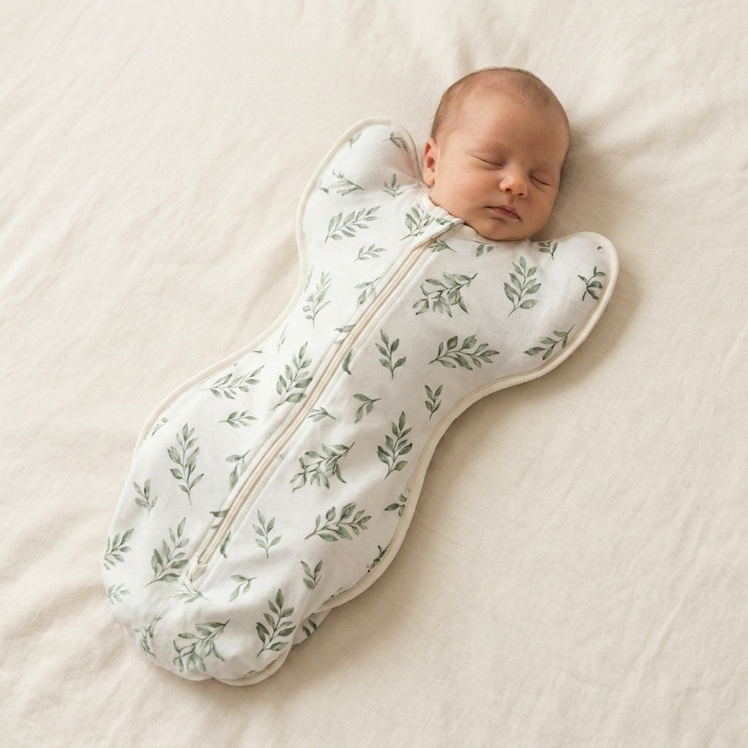 Newborn sleeping in the CradleUp arms-up swaddle, sage leaf print