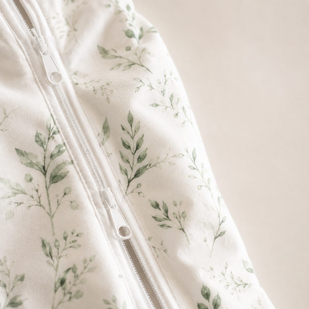 Close-up of the CradleUp swaddle's two-way zipper and soft leaf-print cotton